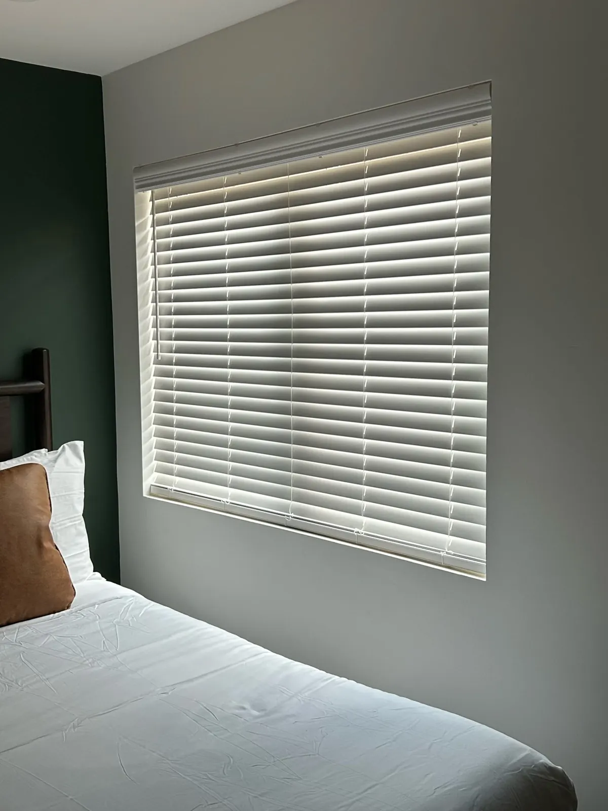 White faux wood blinds on a bedroom window with a dark accent wall in a Dallas rental