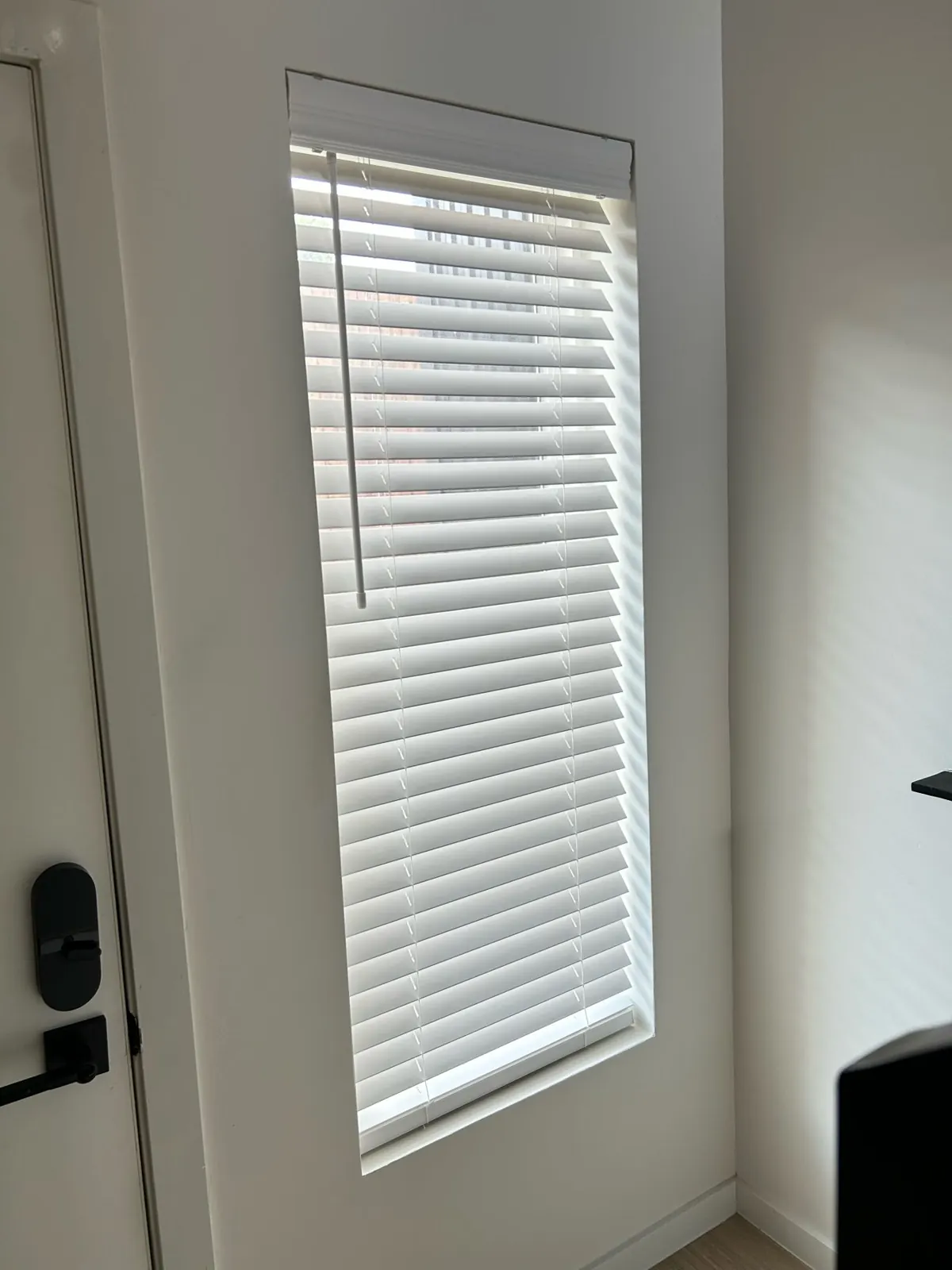 Narrow white faux wood blind on a tall window beside an entry door in a Dallas rental unit