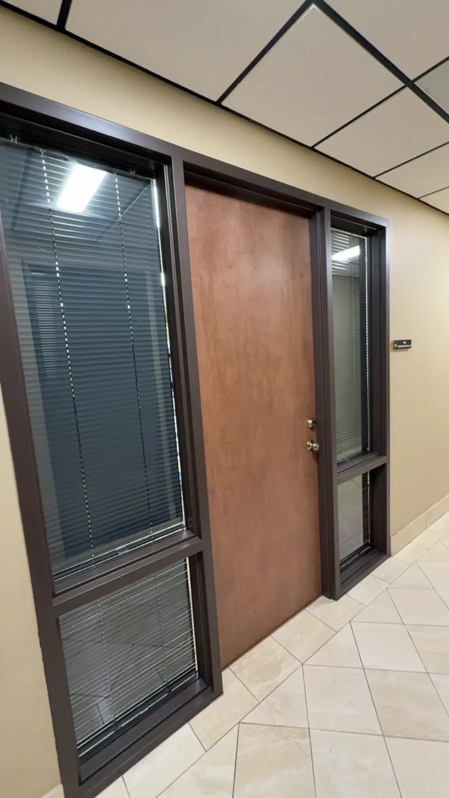 Dark blinds on glass sidelights beside a wood office door in a Frisco, TX office