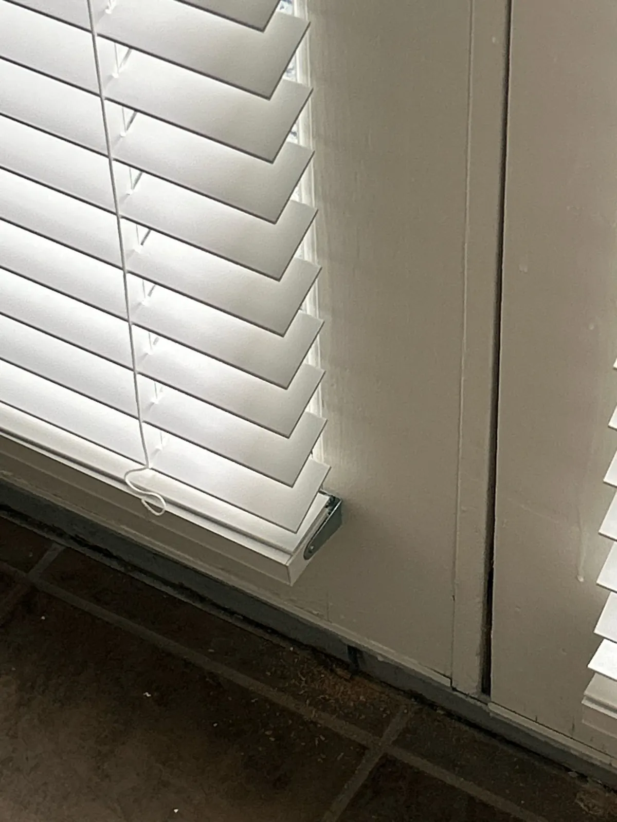 Close-up of a white faux wood blind bottom rail on a door panel