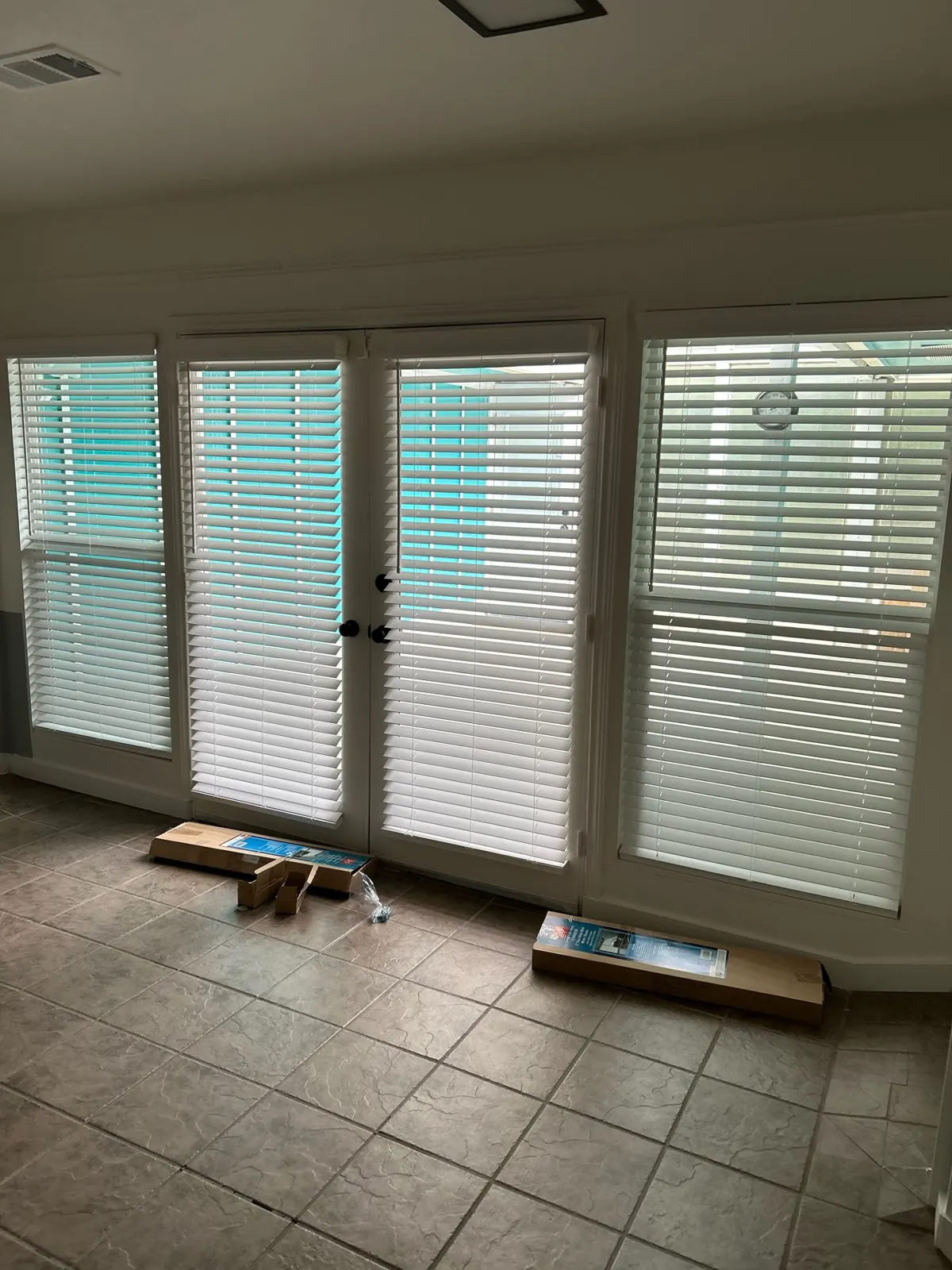 White faux wood blinds on French doors and windows in an Irving living room during install