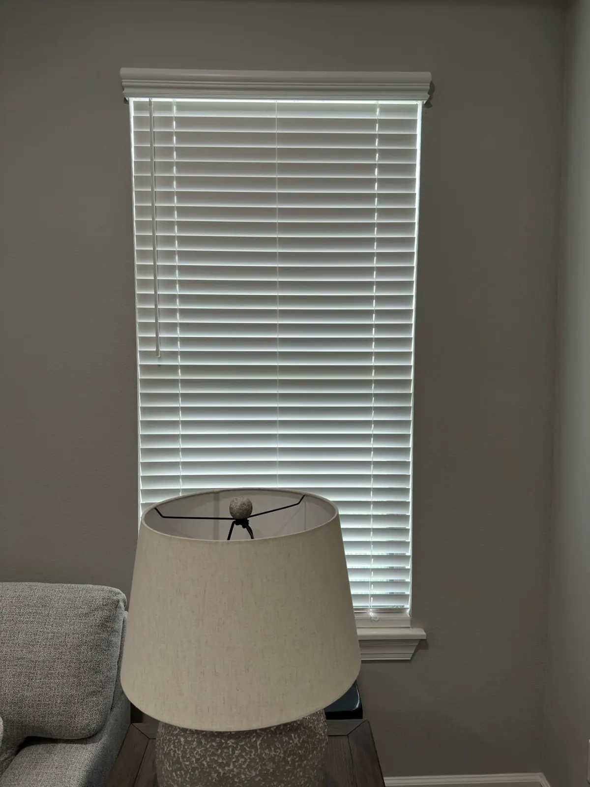 Tall white faux wood blind behind a table lamp in a Tampa living room