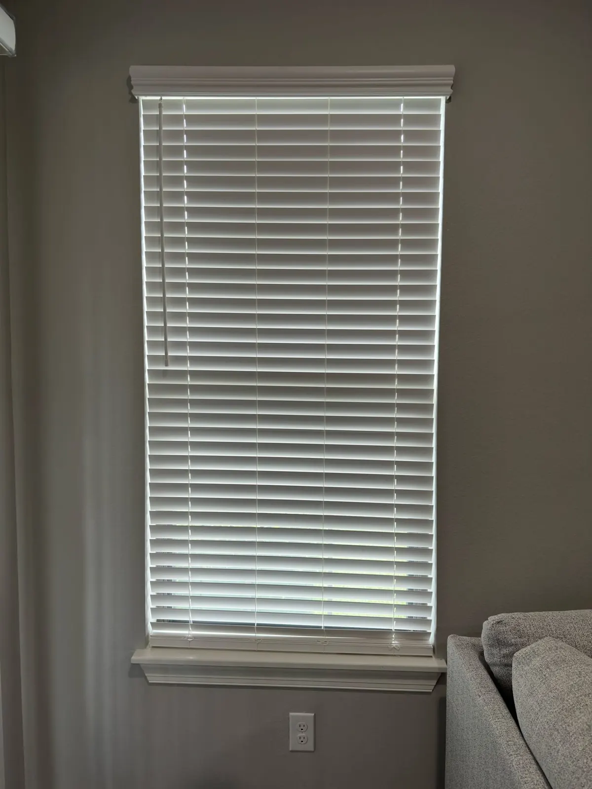 White faux wood blind on a tall living room window, installed by the homeowner