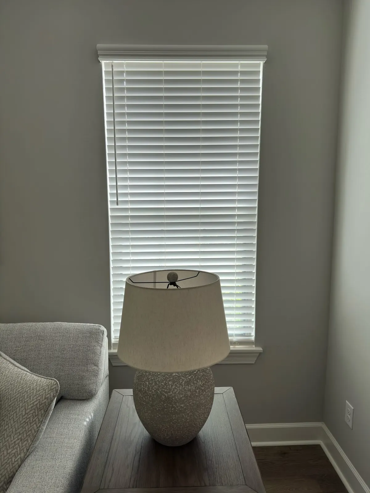 White faux wood blind on a narrow window beside a lamp in Tampa, FL